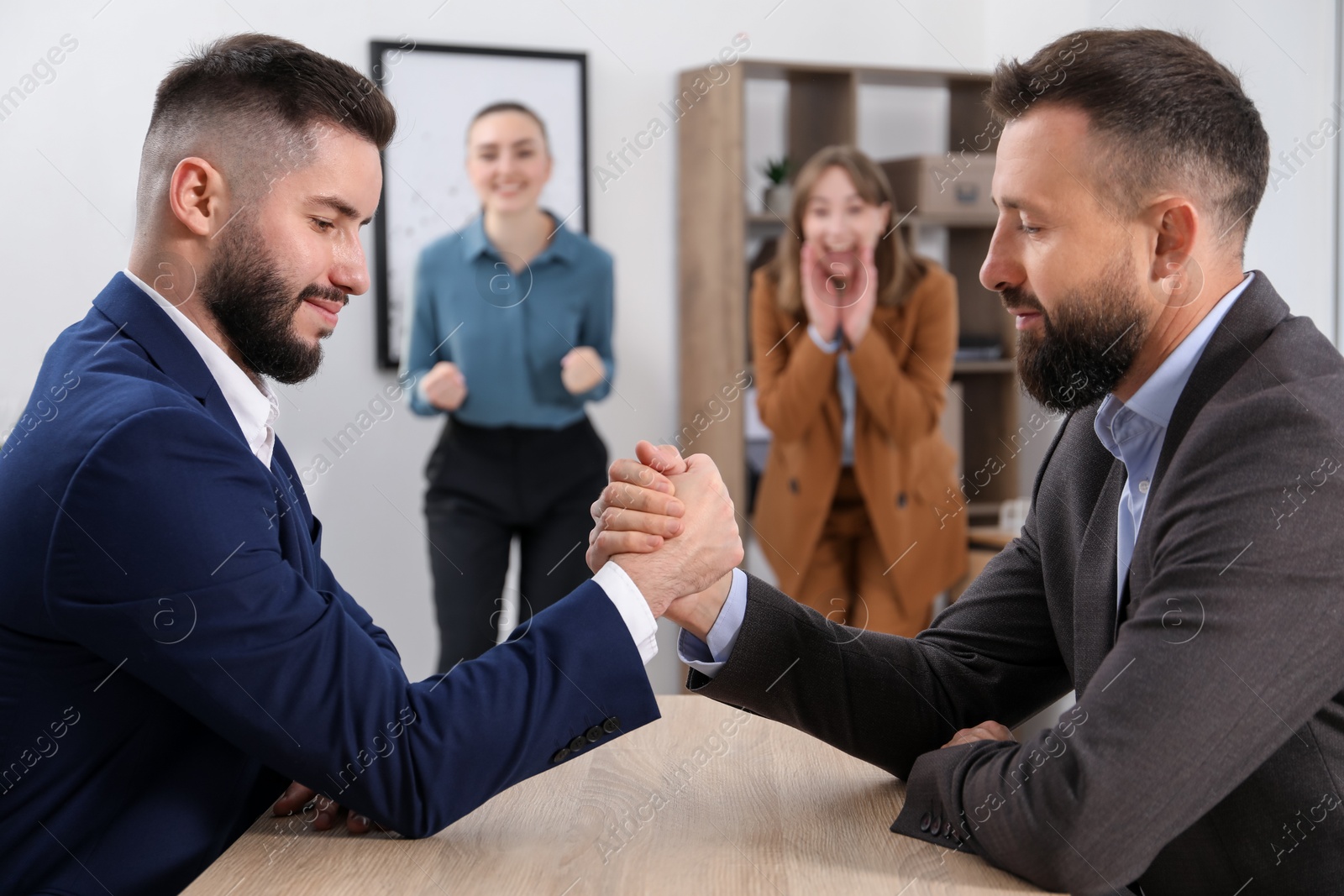 Businessmen arm wrestling at wooden table in office, selective focus Photo of Businessmen arm wrestling at wooden table in office, selective focus