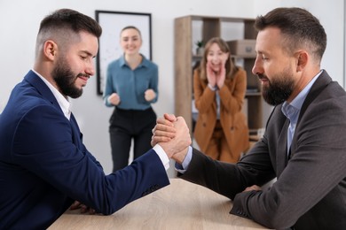 Photo of Businessmen arm wrestling at wooden table in office, selective focus