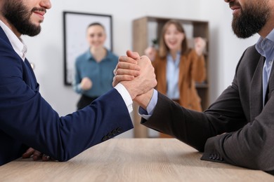Photo of Businessmen arm wrestling at wooden table in office, selective focus