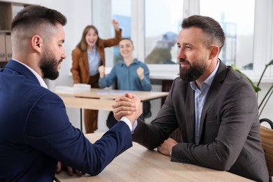 Photo of Businessmen arm wrestling at wooden table in office, selective focus