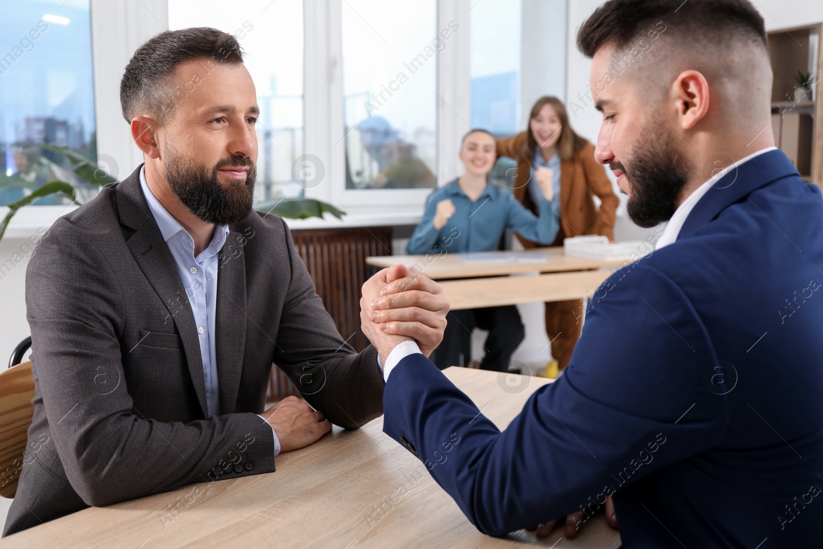 Businessmen arm wrestling at wooden table in office, selective focus Photo of Businessmen arm wrestling at wooden table in office, selective focus