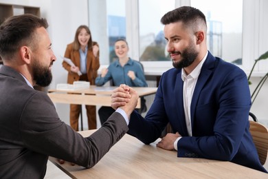Photo of Businessmen arm wrestling at wooden table in office, selective focus