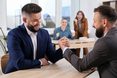 Photo of Businessmen arm wrestling at wooden table in office, selective focus