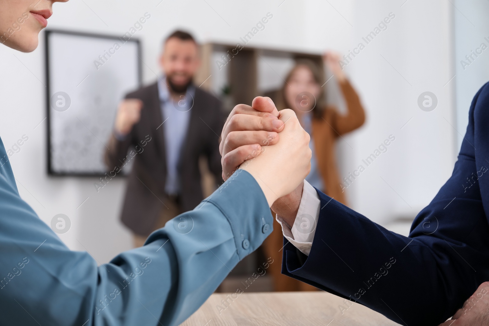 Businesspeople arm wrestling at table in office, selective focus Photo of Businesspeople arm wrestling at table in office, selective focus