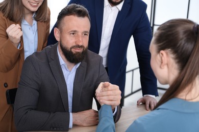 Photo of Businesspeople arm wrestling at wooden table in office