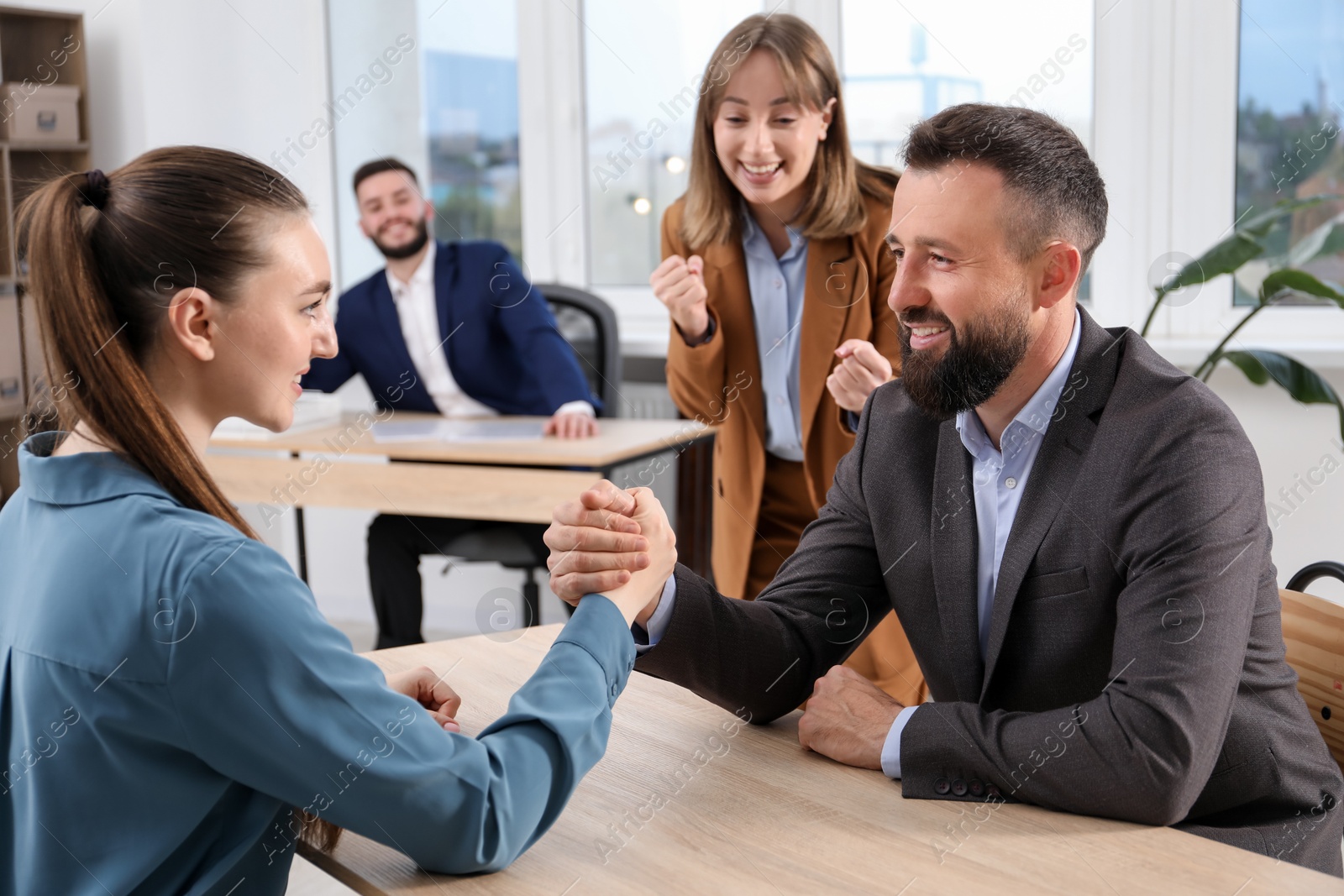 Businesspeople arm wrestling at wooden table in office Photo of Businesspeople arm wrestling at wooden table in office