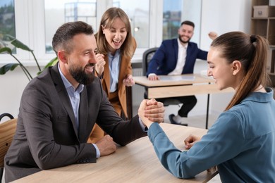 Photo of Businesspeople arm wrestling at wooden table in office