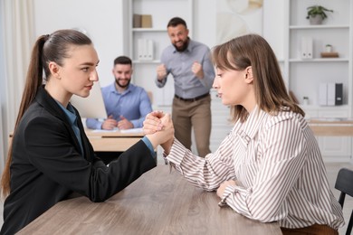 Photo of Businesswomen arm wrestling at wooden table in office, selective focus