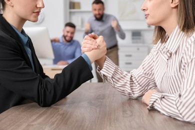 Photo of Businesswomen arm wrestling at wooden table in office, selective focus