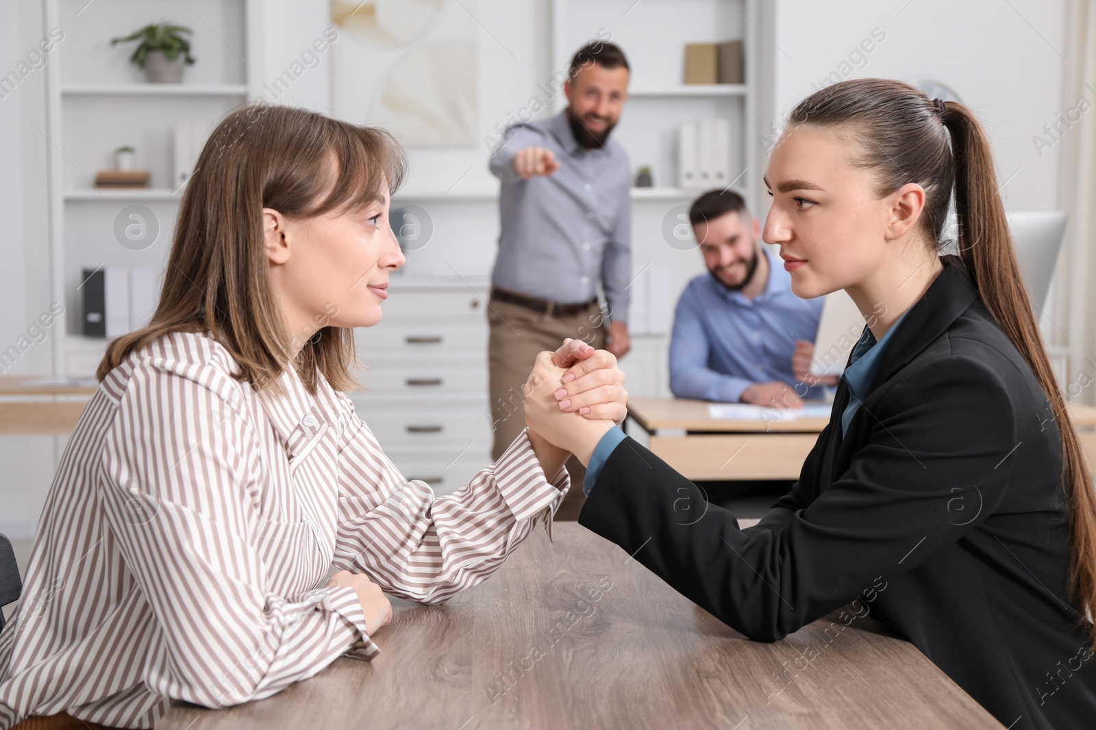 Businesswomen arm wrestling at wooden table in office, selective focus Photo of Businesswomen arm wrestling at wooden table in office, selective focus