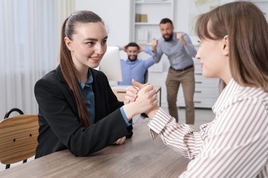 Photo of Businesswomen arm wrestling at wooden table in office, selective focus