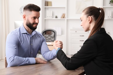 Photo of Businesspeople arm wrestling at wooden table in office