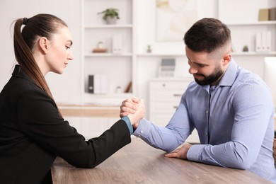 Photo of Businesspeople arm wrestling at wooden table in office