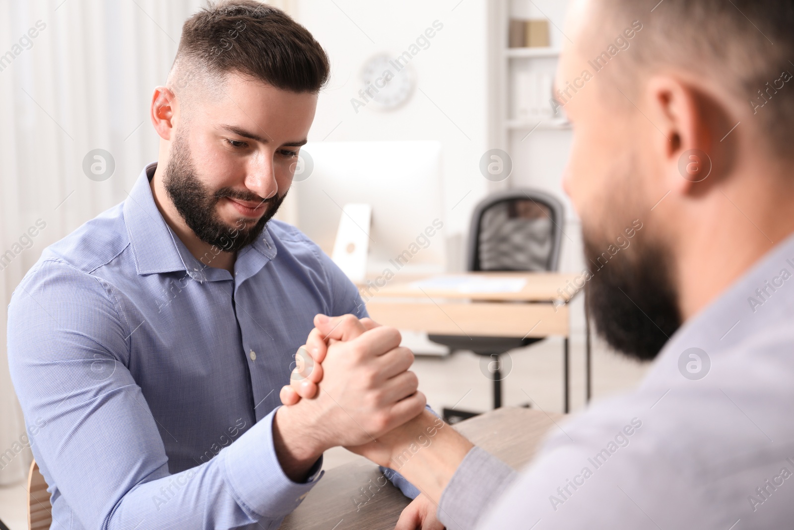 Businessmen arm wrestling at table in office Photo of Businessmen arm wrestling at table in office