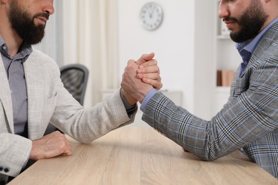 Photo of Businessmen arm wrestling at wooden table in office, closeup