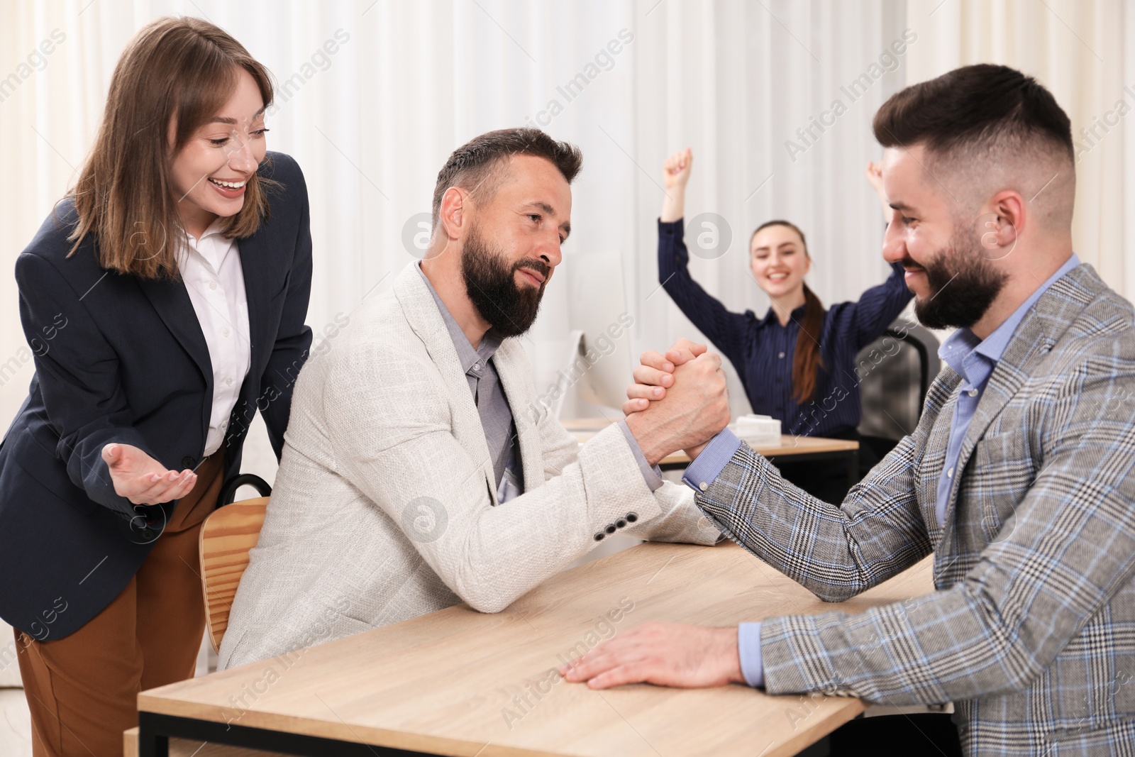 Businessmen arm wrestling at wooden table in office Photo of Businessmen arm wrestling at wooden table in office