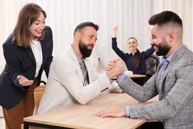 Photo of Businessmen arm wrestling at wooden table in office