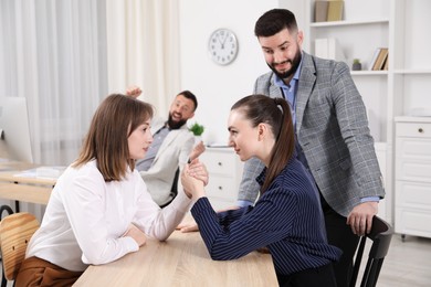 Photo of Businesswomen arm wrestling at wooden table in office