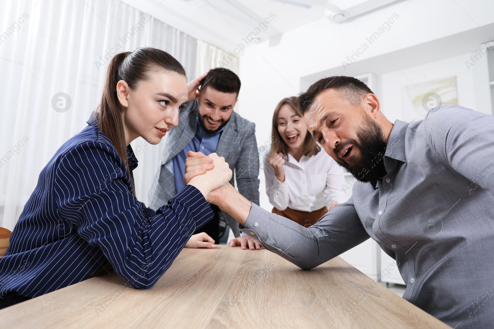 Businesspeople arm wrestling at wooden table in office Photo of Businesspeople arm wrestling at wooden table in office