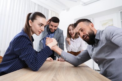 Photo of Businesspeople arm wrestling at wooden table in office
