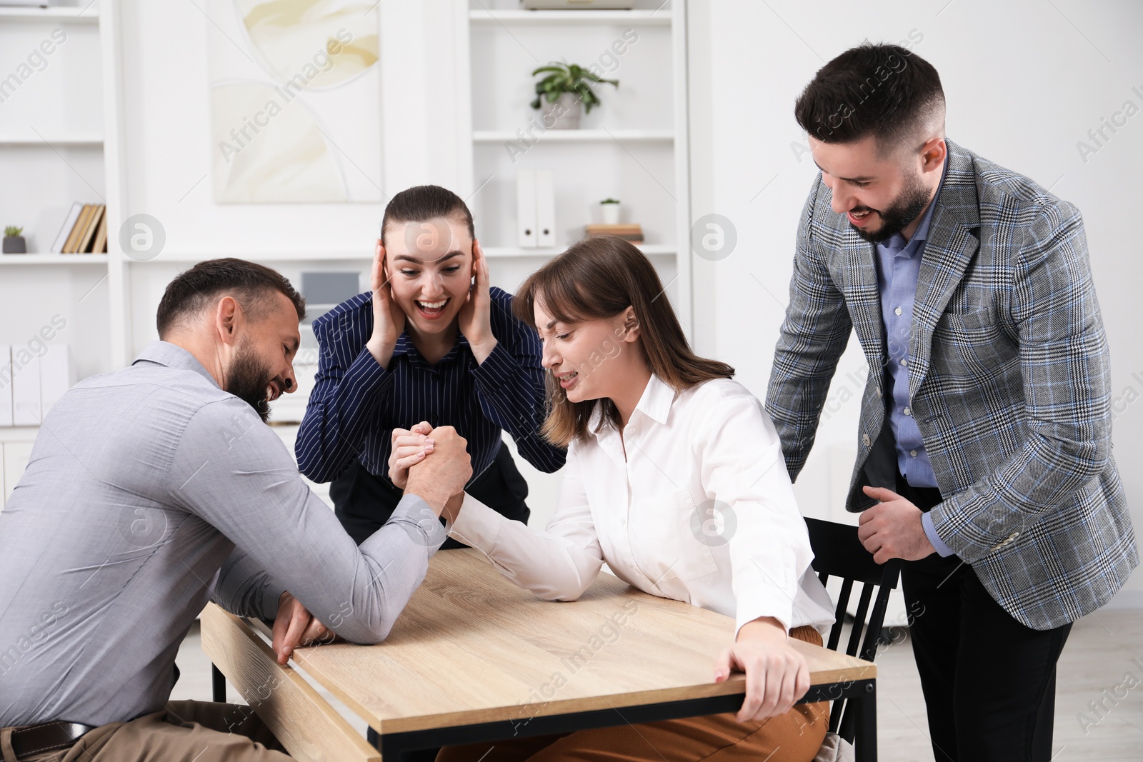 Businesspeople arm wrestling at wooden table in office Photo of Businesspeople arm wrestling at wooden table in office
