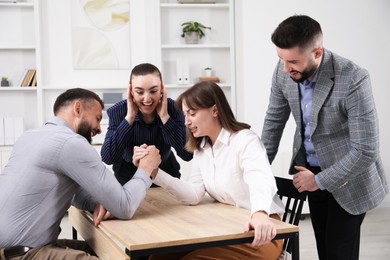 Photo of Businesspeople arm wrestling at wooden table in office