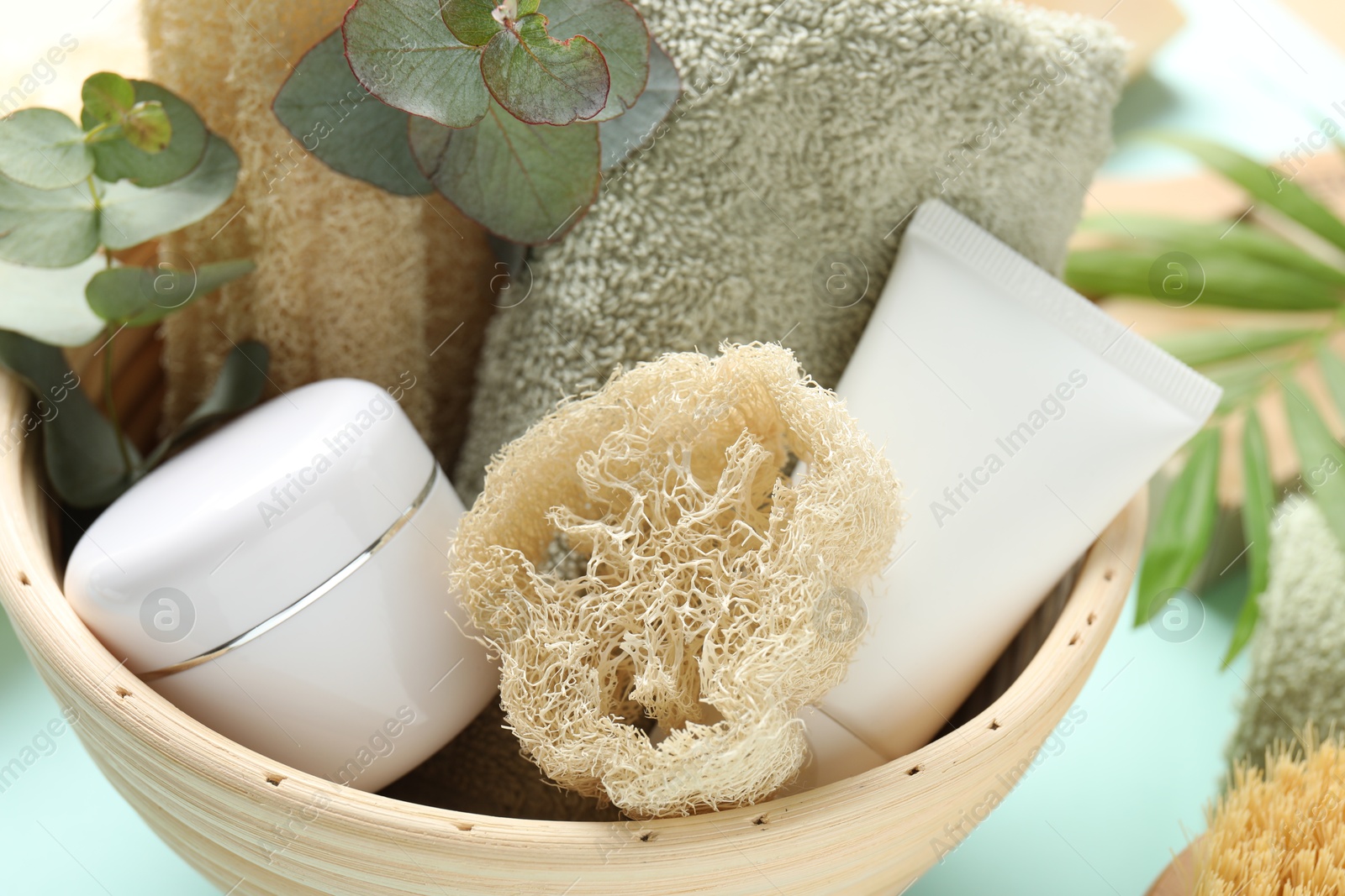 Loofah sponges, cosmetic products, towel and floral decor on light blue background, closeup Photo of Loofah sponges, cosmetic products, towel and floral decor on light blue background, closeup