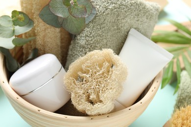 Photo of Loofah sponges, cosmetic products, towel and floral decor on light blue background, closeup