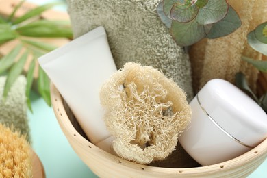 Photo of Loofah sponges, cosmetic products, towel and floral decor on light blue background, closeup