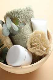 Photo of Loofah sponges, cosmetic products, towel and floral decor in bowl on beige background, above view