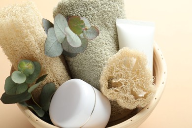 Photo of Loofah sponges, cosmetic products, towel and floral decor in bowl on beige background, closeup