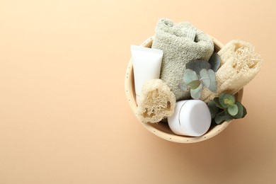 Photo of Loofah sponges, cosmetic products, towel and floral decor in bowl on beige background, top view. Space for text