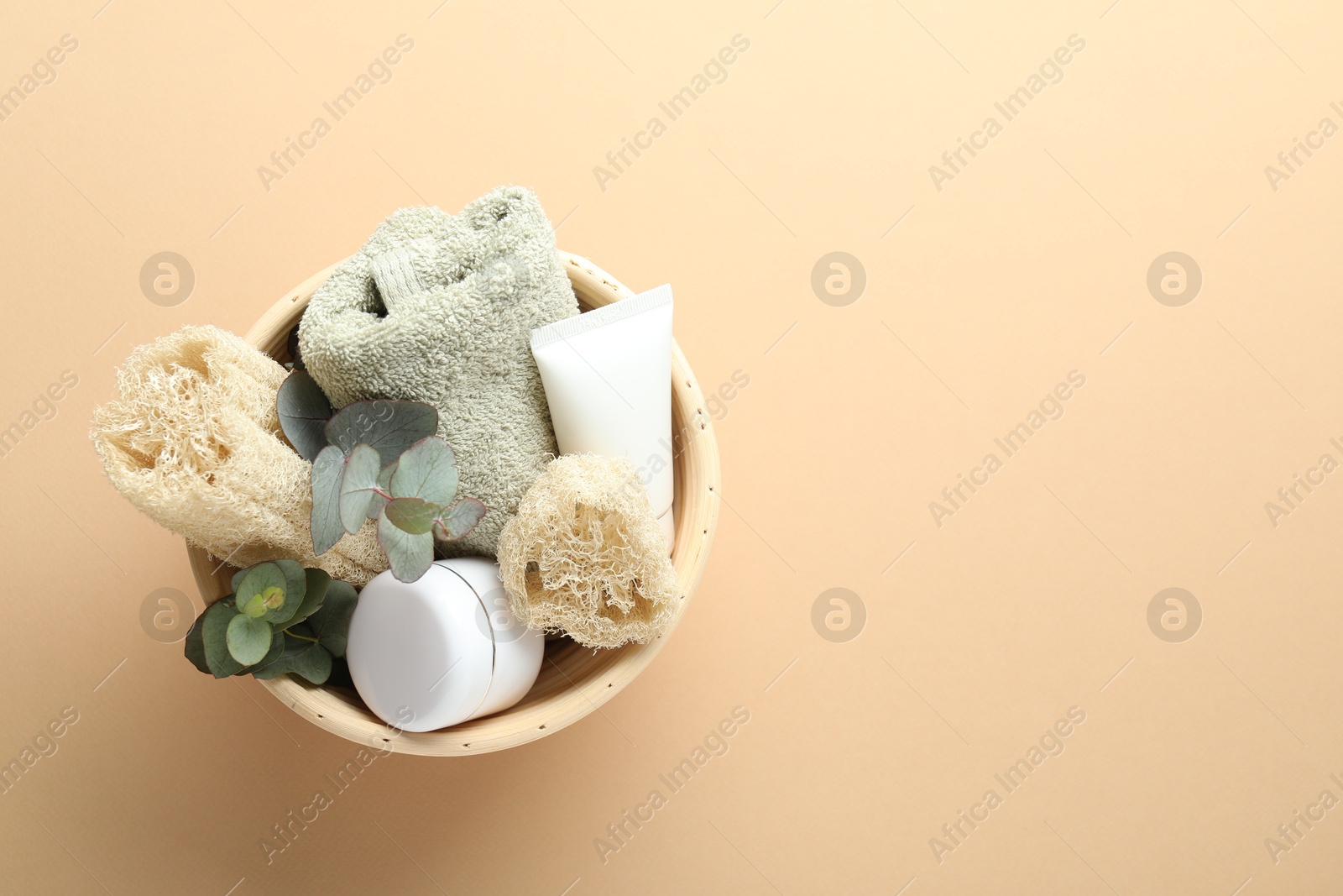 Loofah sponges, cosmetic products, towel and floral decor in bowl on beige background, top view. Space for text Photo of Loofah sponges, cosmetic products, towel and floral decor in bowl on beige background, top view. Space for text