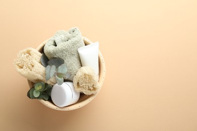 Photo of Loofah sponges, cosmetic products, towel and floral decor in bowl on beige background, top view. Space for text