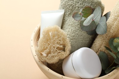 Photo of Loofah sponges, cosmetic products, towel and floral decor in bowl on beige background, closeup. Space for text