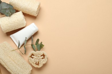 Photo of Loofah sponges, cosmetic product and eucalyptus leaves on beige background, flat lay. Space for text