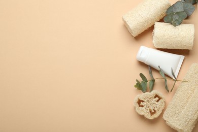 Photo of Loofah sponges, cosmetic product and eucalyptus leaves on beige background, flat lay. Space for text