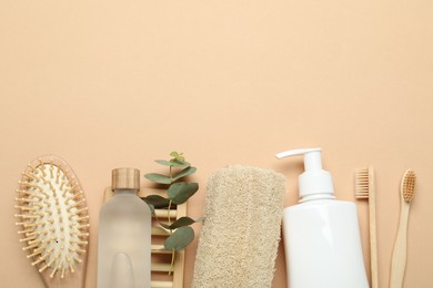 Photo of Loofah sponges, cosmetic products, toothbrushes, brush and eucalyptus branch on beige background, flat lay. Space for text