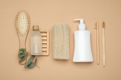 Photo of Loofah sponges, cosmetic products, toothbrushes, brush and eucalyptus branch on beige background, flat lay
