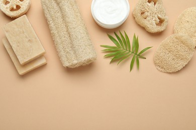 Photo of Loofah sponges, cosmetic product, soap and green twig on beige background, flat lay. Space for text