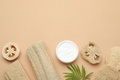 Photo of Loofah sponges, cosmetic product, soap and green twig on beige background, flat lay. Space for text
