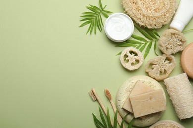 Photo of Natural loofah sponges, cosmetic products, soap, toothbrushes and twigs on green background, flat lay. Space for text