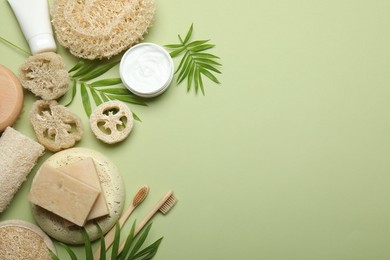 Photo of Natural loofah sponges, cosmetic products, soap, toothbrushes and twigs on green background, flat lay. Space for text