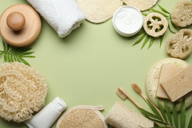 Photo of Frame of natural loofah sponges, cosmetic products, soap, toothbrushes, towel and twigs on green background, flat lay. Space for text