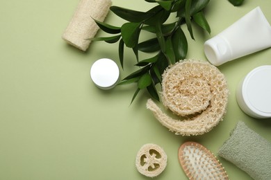 Photo of Natural loofah sponges, cosmetic products, brush, towel and leaves on green background, flat lay. Space for text