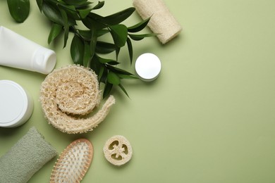 Photo of Natural loofah sponges, cosmetic products, brush, towel and leaves on green background, flat lay. Space for text