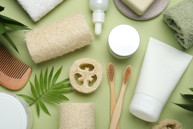 Photo of Natural loofah sponges, cosmetic products, toothbrushes, towel and floral decor on green background, flat lay