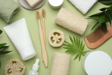 Photo of Natural loofah sponges, cosmetic products, toothbrushes, towel and floral decor on green background, flat lay