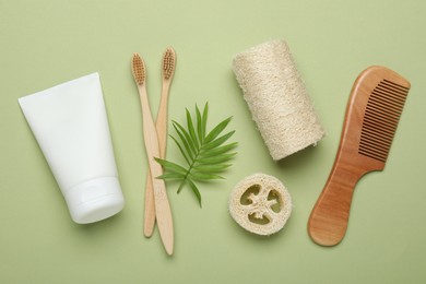 Photo of Natural loofah sponges, cosmetic product, toothbrushes, comb and twig on green background, flat lay