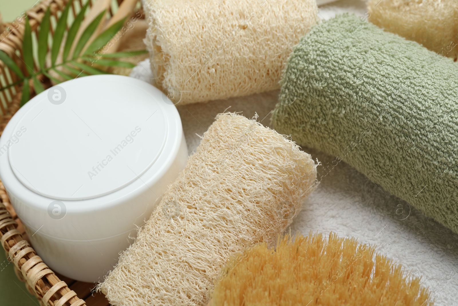 Natural loofah sponges, cosmetic product, towels, brush and twig in basket, closeup Photo of Natural loofah sponges, cosmetic product, towels, brush and twig in basket, closeup
